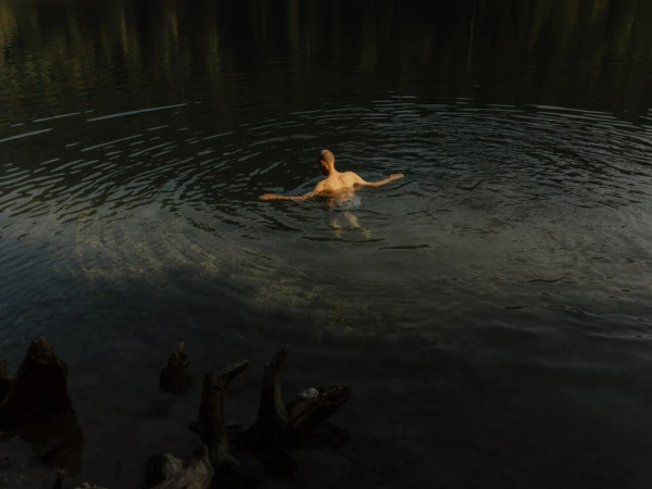 Man swimming in a dark mountain lake creating ripples in the water, captured from above by Grant Harder