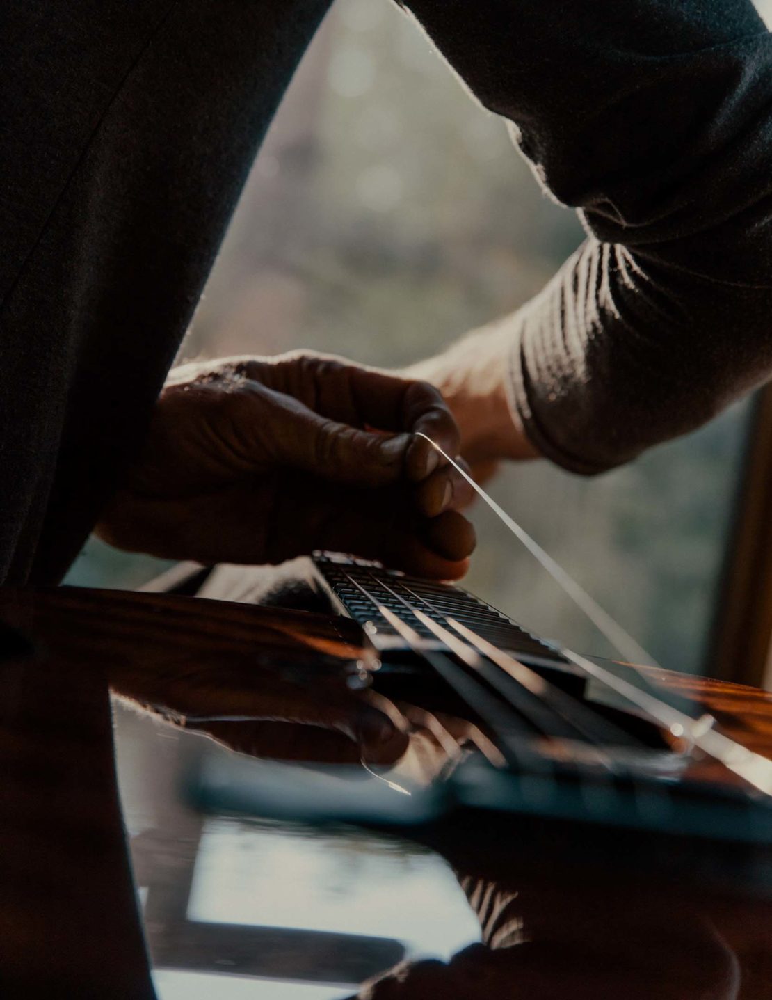 Close-up of a person changing strings on an acoustic guitar, bathed in soft, natural light from a nearby window. Musical instrument maintenance.
