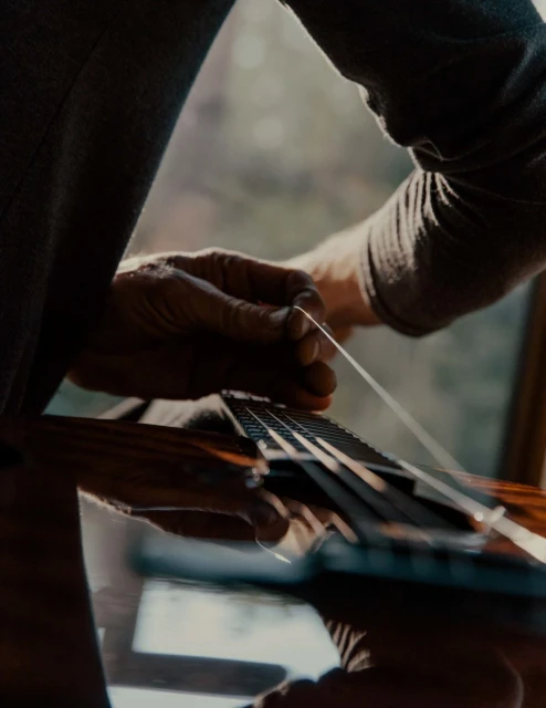 Close-up of a person changing strings on an acoustic guitar, bathed in soft, natural light from a nearby window. Musical instrument maintenance.