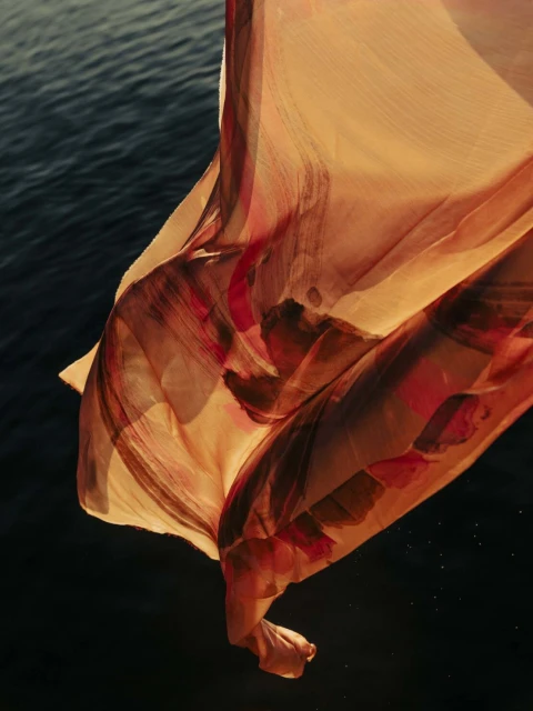 Abstract art with a lightweight, peach-colored fabric billowing above dark-blue water, creating a dreamy and ethereal visual.