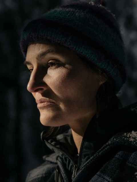 Close-up of a woman in a wool hat looking left. She is wearing a dark jacket with a gray, patterned fleece and is outside in soft light.