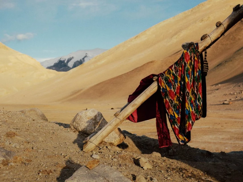 Colorful textile draped on a wooden structure in a desert landscape with mountains in the distance, creating a striking contrast.