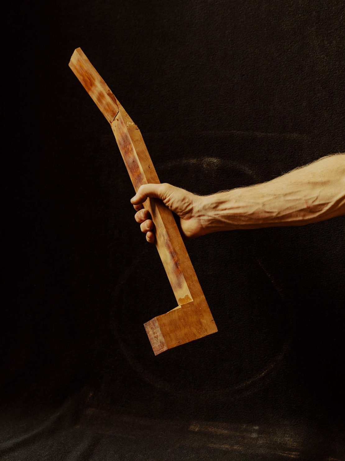 An adult hand holds a section of wooden guitar neck on a black background, focusing on texture and natural wood tones in a close-up shot.