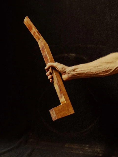 An adult hand holds a section of wooden guitar neck on a black background, focusing on texture and natural wood tones in a close-up shot.