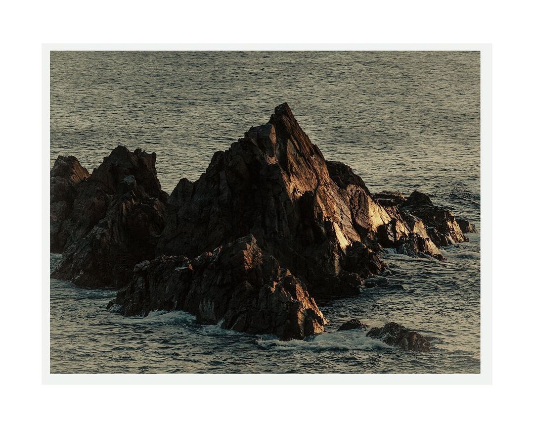 Coastal rock formation in ocean water, with natural lighting and ocean waves in the background under a hazy sky.