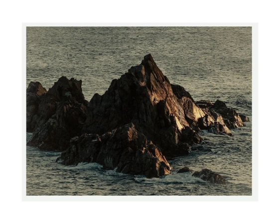 Coastal rock formation in ocean water, with natural lighting and ocean waves in the background under a hazy sky.