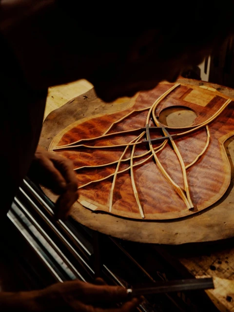 Adult creating a guitar's body with wood pieces and hand tools in a workshop with dim lighting and a close-up shot.