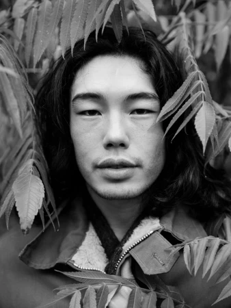 Close-up black and white portrait of a man with long dark hair framed by foliage by Grant Harder