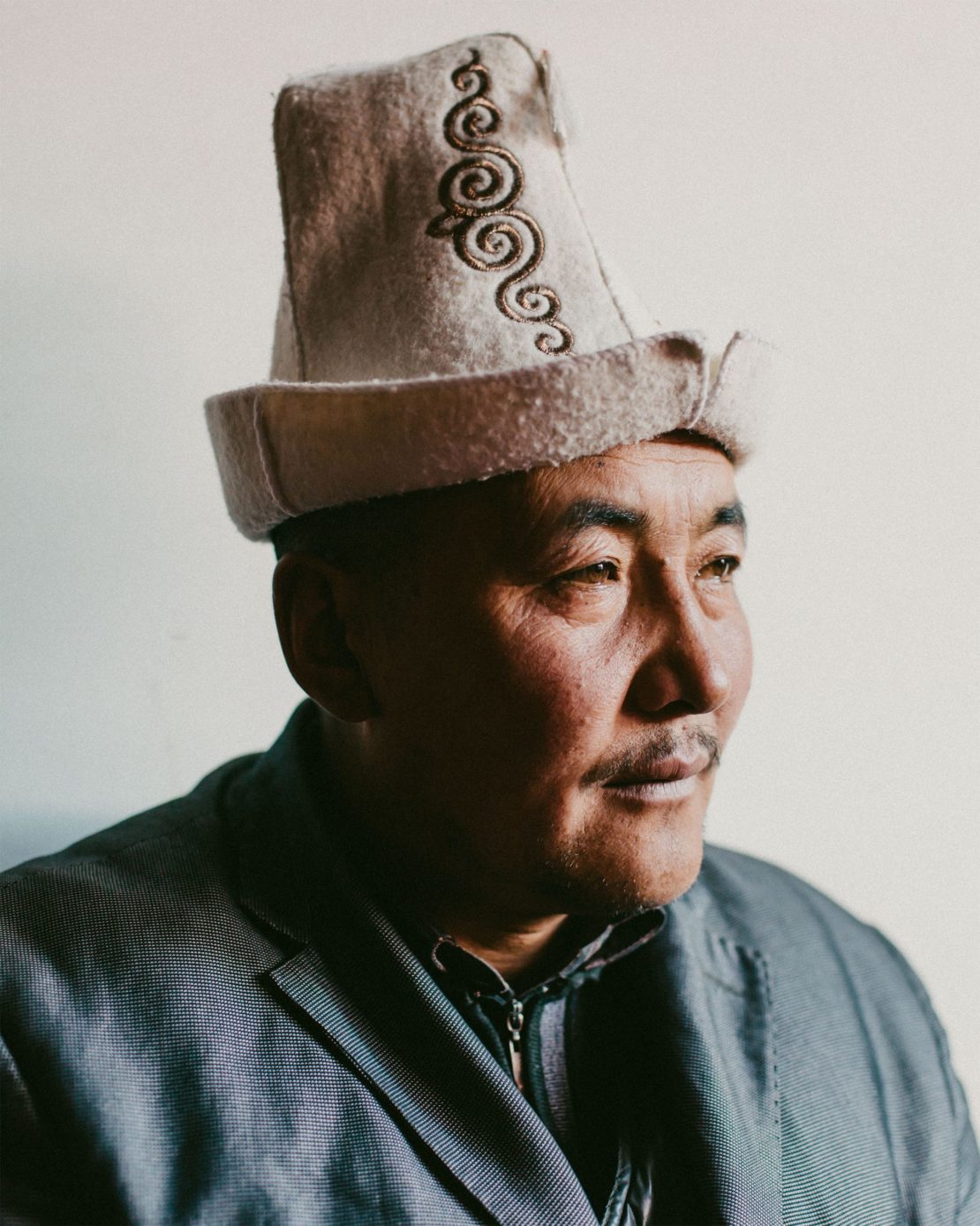 Portrait of an adult male wearing a traditional felt hat with embroidery against a neutral background in a close-up, studio shot.