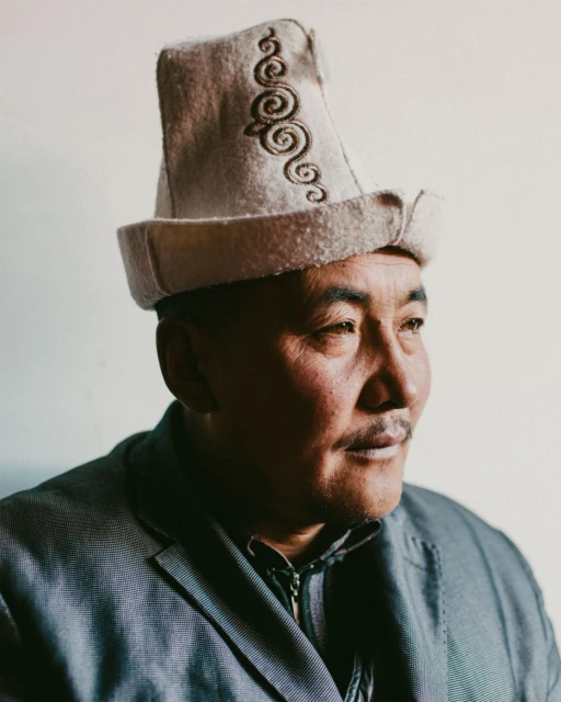 Portrait of an adult male wearing a traditional felt hat with embroidery against a neutral background in a close-up, studio shot.