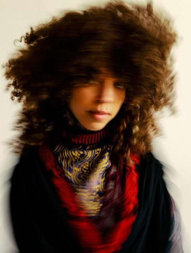 Woman with curly hair and patterned top, blurred motion effect, indoors. Portrait of a fashionable person with a distinctive hairstyle.