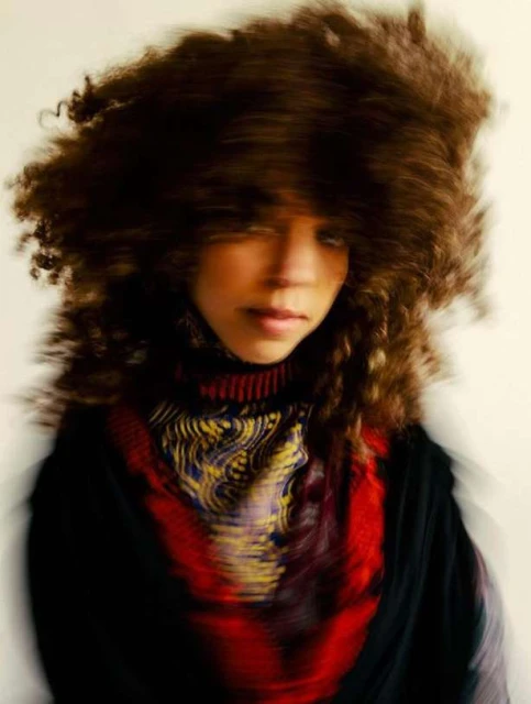 Woman with curly hair and patterned top, blurred motion effect, indoors. Portrait of a fashionable person with a distinctive hairstyle.