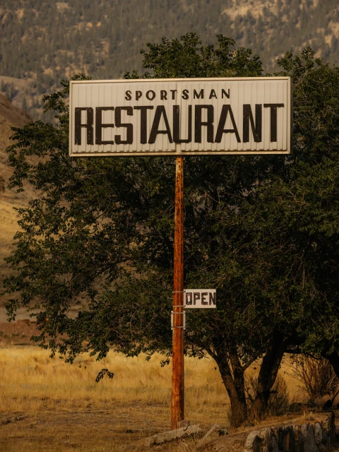 Vintage roadside sign for Sportsman Restaurant with a weathered look surrounded by trees and a rural landscape.