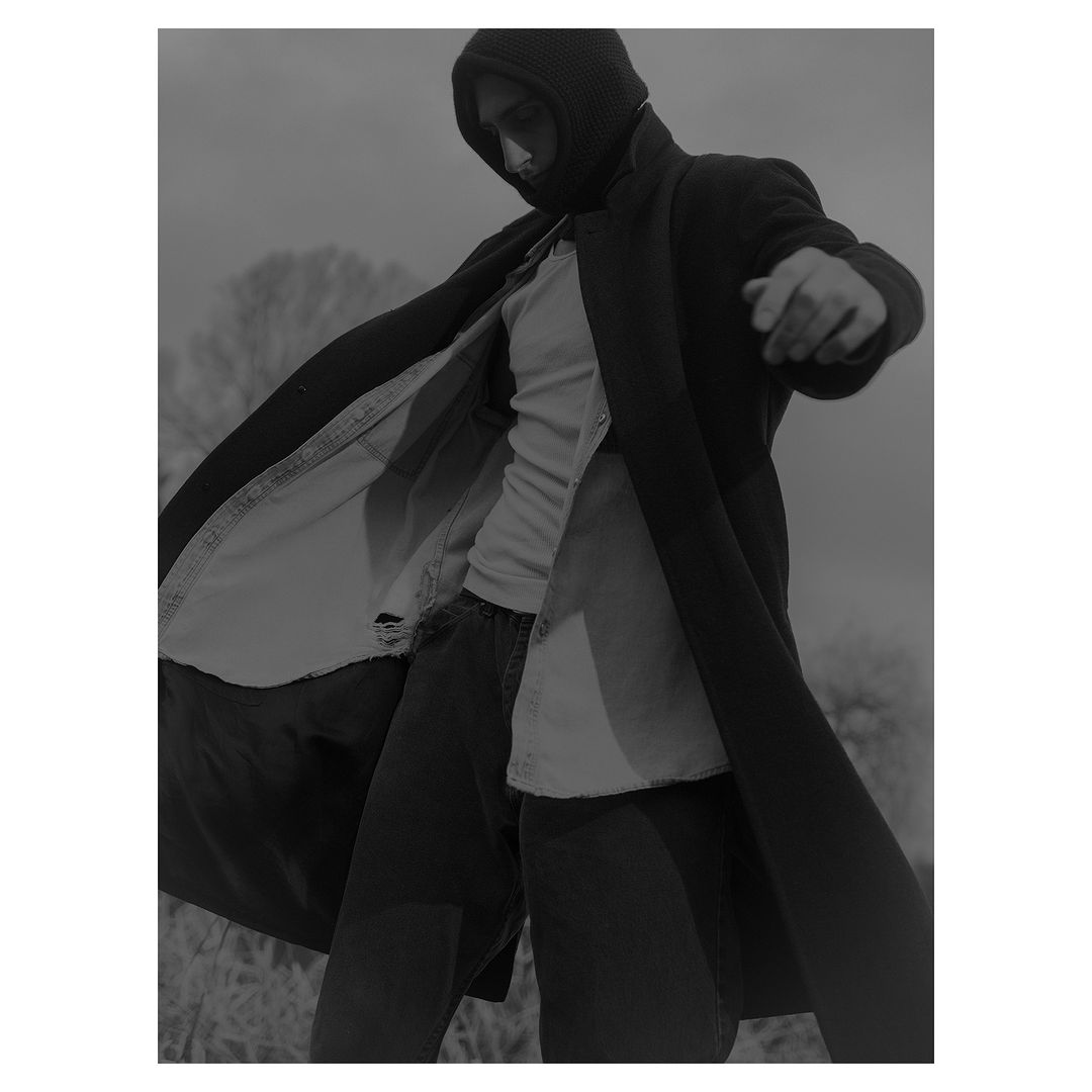 Man wearing a dark hooded coat, light t-shirt, and dark pants outdoors by Grant Harder