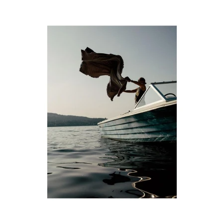 A person standing on a boat on a lake, holding up a fabric banner against an overcast sky, captured by Grant Harder