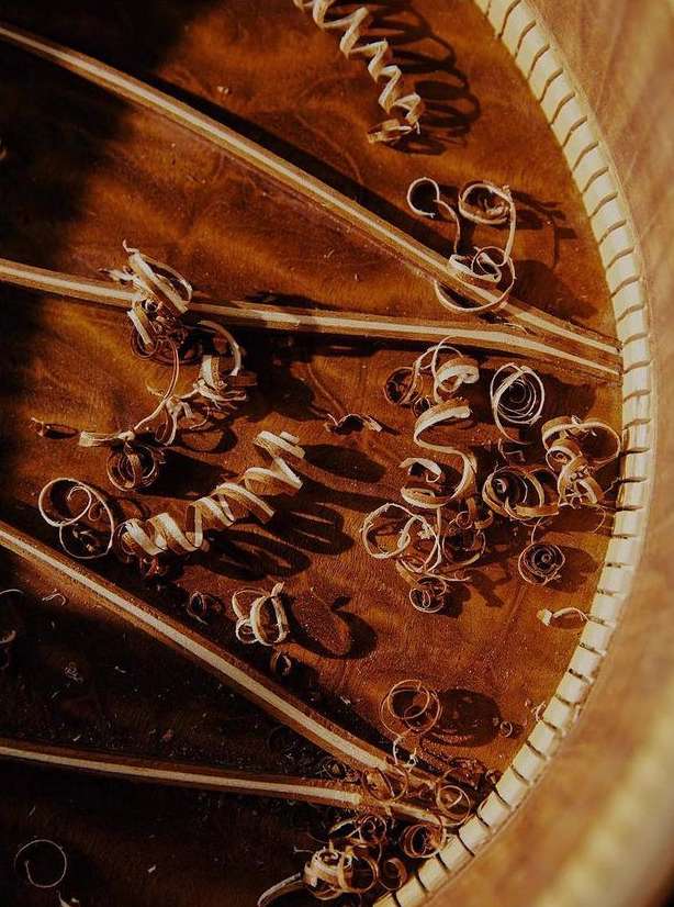 Close-up of a guitar soundboard being crafted, showing wood shavings and rosette detailing, focusing on the instrument's construction.
