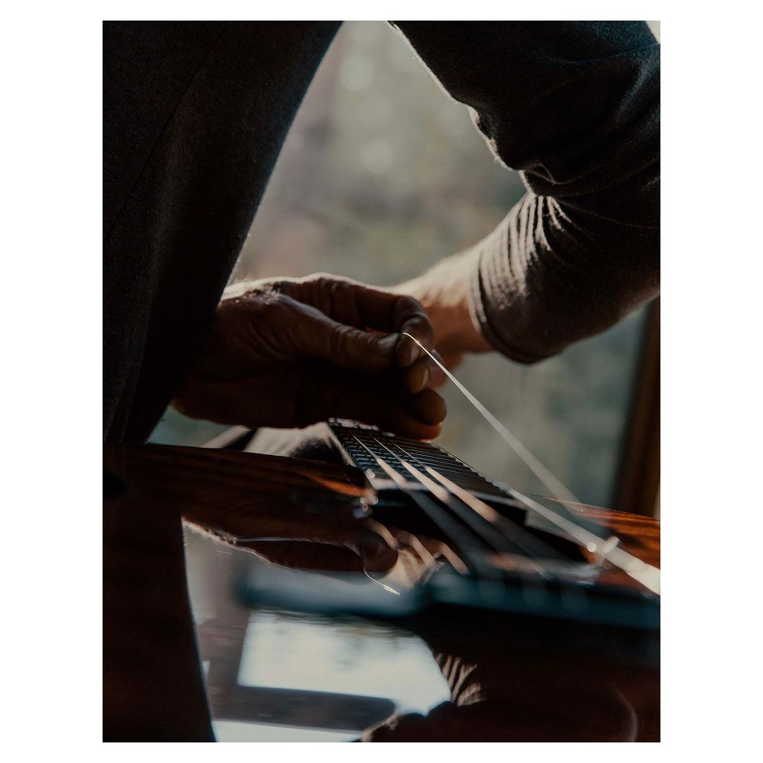 Close-up of person's hands replacing a guitar string on an acoustic guitar indoors with natural lighting and shallow depth of field.