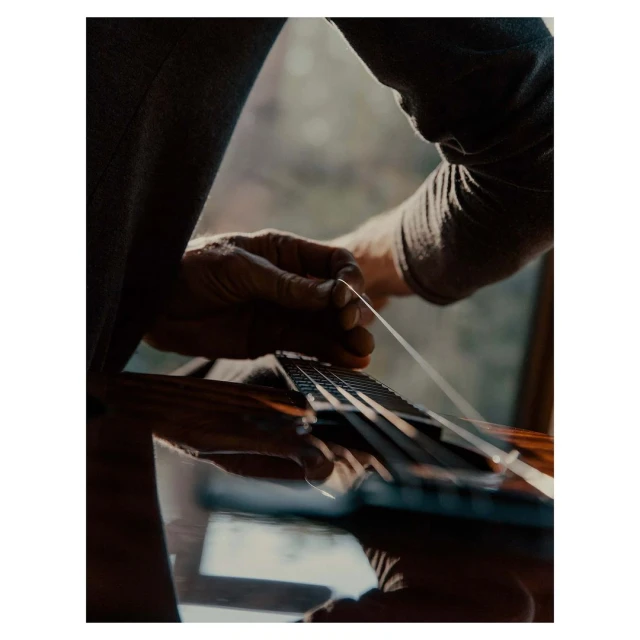 Close-up of person's hands replacing a guitar string on an acoustic guitar indoors with natural lighting and shallow depth of field.