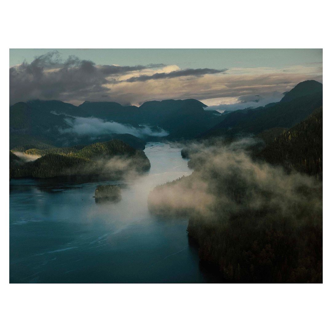 Aerial view of a misty river winding through dark forested mountains under a cloudy twilight sky in Vancouver
