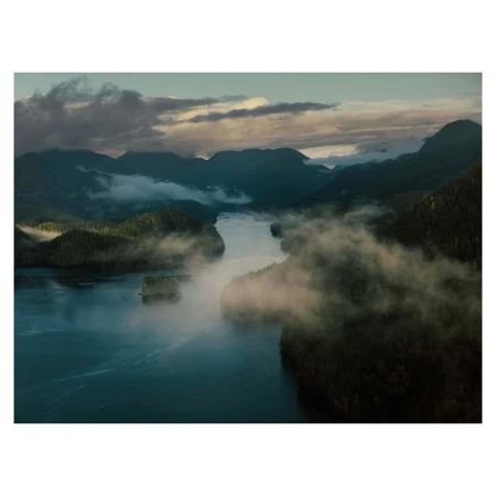 Aerial view of a misty river winding through dark forested mountains under a cloudy twilight sky in Vancouver