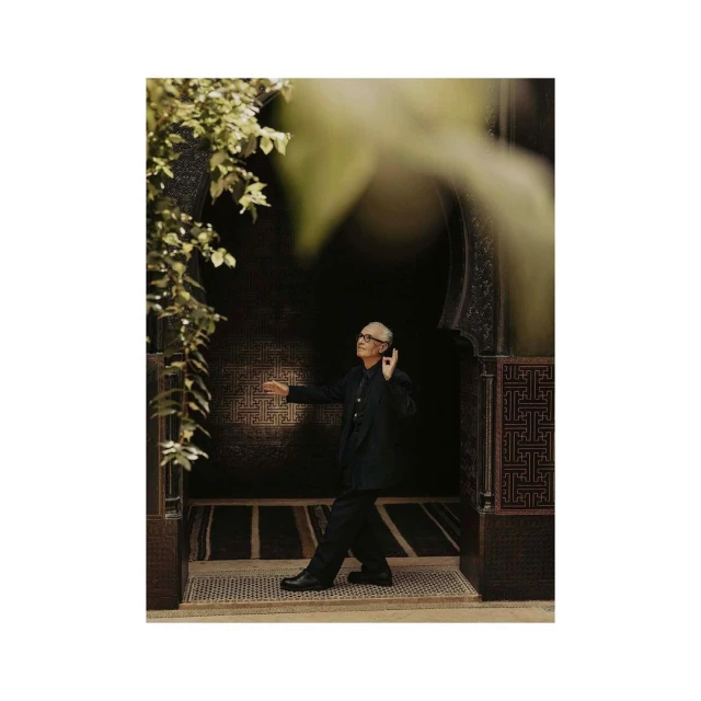 Elegant man in a dark suit poses within a Moroccan-style archway, framed by lush greenery and intricately patterned architectural details.