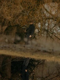 Man in a dark coat standing near bare winter trees with a water reflection below, photographed by Grant Harder