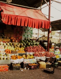Vibrant fruit market stall in Vancouver stacked with watermelons, apples, oranges, and bananas under a red awning