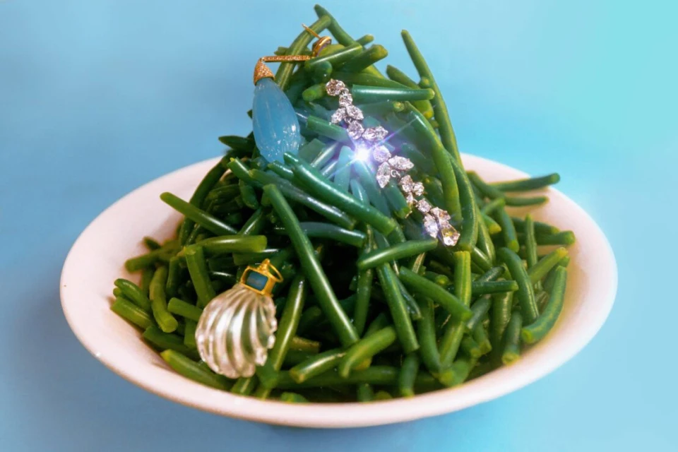 Still life composition featuring green beans on a white plate adorned with jewellery against a light blue background in horizontal format.