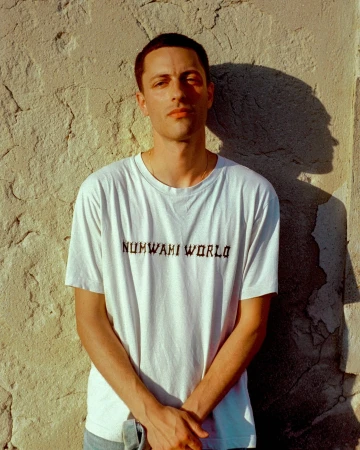 Portrait of a man in a white printed t shirt standing against a textured concrete wall with a harsh shadow