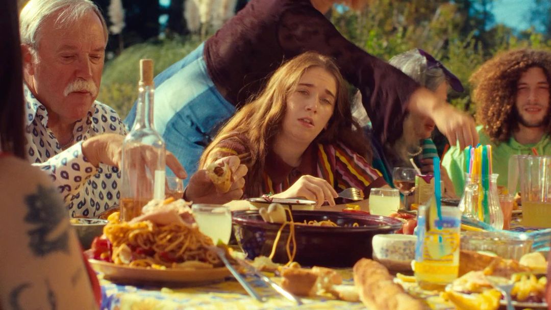 Group of diverse people gathered around an outdoor dining table laden with food and wine bottles captured by Kamila K Stanley.