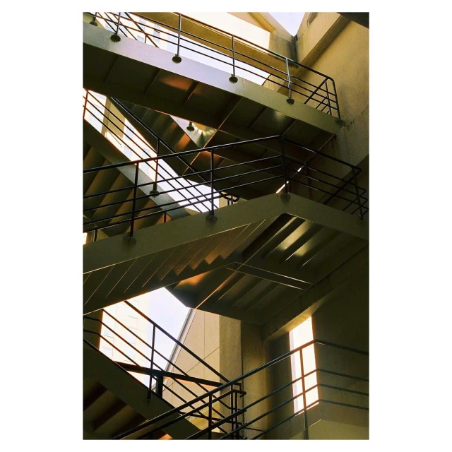 Abstract view of an architectural staircase with multiple landings and black metal railings in a concrete building with natural light.