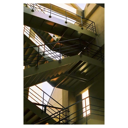 Abstract view of an architectural staircase with multiple landings and black metal railings in a concrete building with natural light.