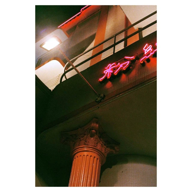Low-angle shot showcases a column supporting an overhang, bathed in the warm glow of neon signage and artificial lighting at night.