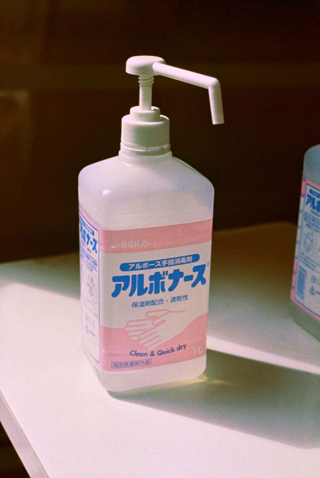 Bottle of Japanese hand sanitizer with pump dispenser and pink label on a white surface in a room with brown walls.