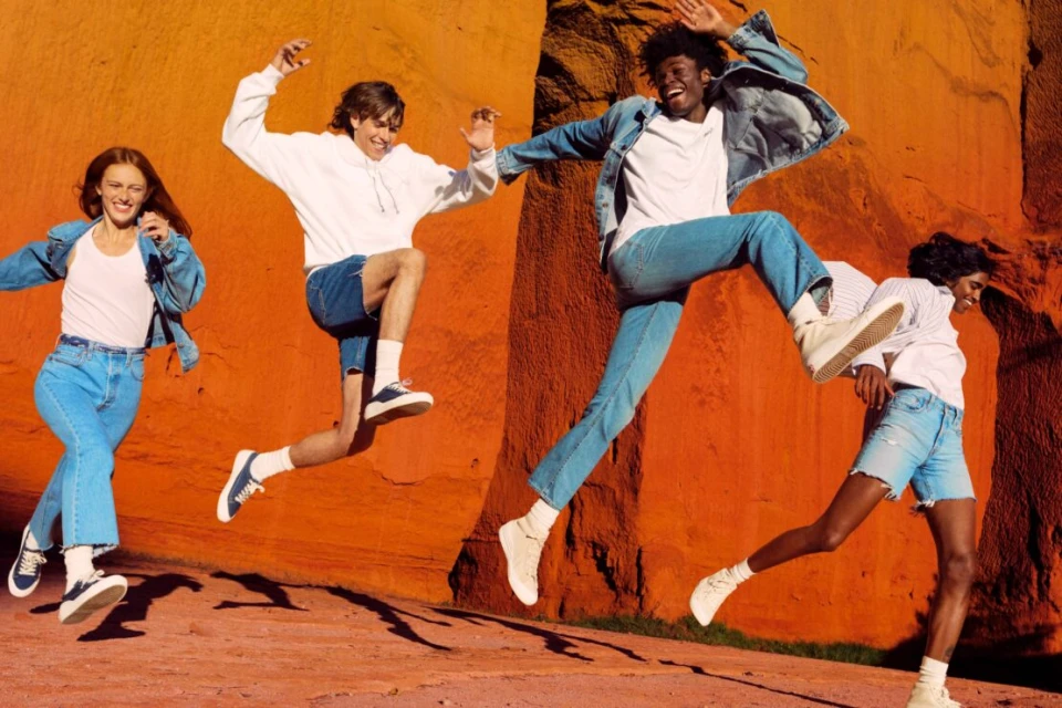 Four young adults joyfully leap against a vibrant orange canyon backdrop, showcasing casual denim fashion and capturing a sense of energetic freedom.