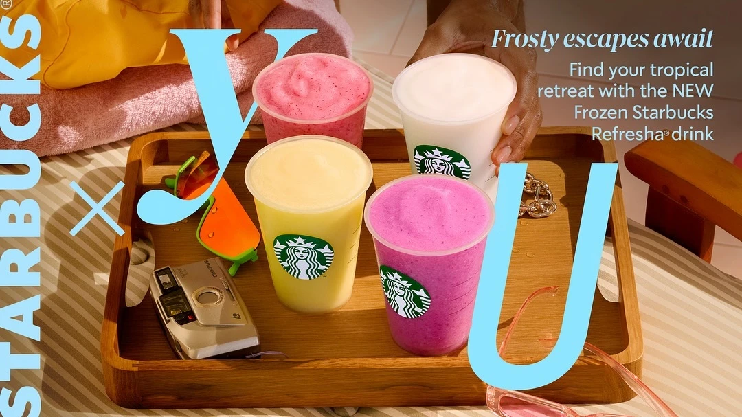 Four Starbucks frozen drinks on a wooden tray with sunglasses, vintage camera, and beach towel in the background. Summer themed.