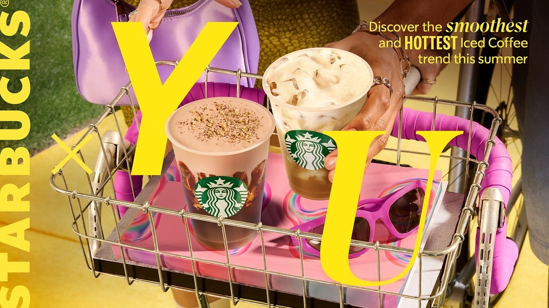 Two iced coffee beverages from Starbucks sit in a bike basket in front of yellow text and a woman holding the basket.