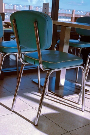 Turquoise diner chairs with chrome metal legs positioned around a table inside a café.