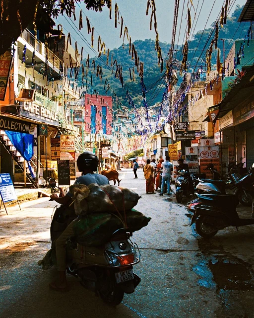 Street view in India showcases a motorcyclist on a scooter, pedestrians, and colorful buildings under a sky strung with decorations.
