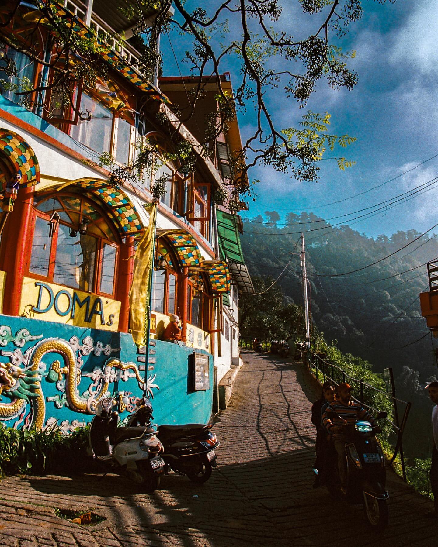 Street view of colourful building in a mountain town with a scooter and people on a moped riding past on a sunny day.