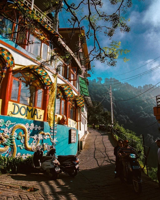 Street view of colourful building in a mountain town with a scooter and people on a moped riding past on a sunny day.