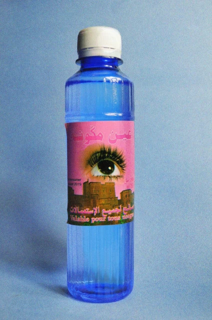 Blue plastic bottle with a pink label featuring an eye and Arabic text, against a light blue background, product shot.