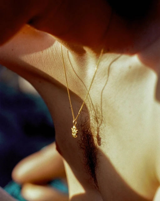 Close-up of an adult wearing a gold necklace with a pendant. The person is lit by natural light, with shadows adding contrast to the skin.