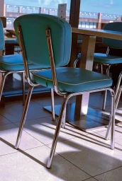 Turquoise diner chairs with chrome metal legs positioned around a table inside a café.