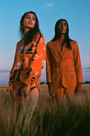 Two models standing in a golden wheat field at sunset, wearing matching orange patterned apparel shot by Kamila K Stanley.