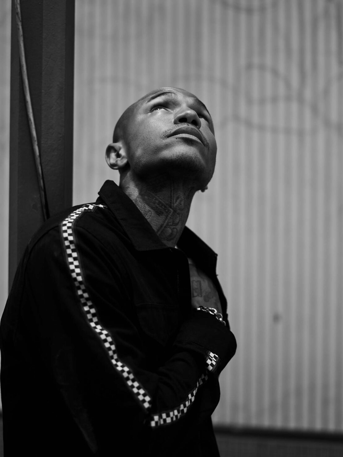 Portrait of a bald man with neck tattoos wearing a black checkered jacket looking upward, by Lauren Dukoff