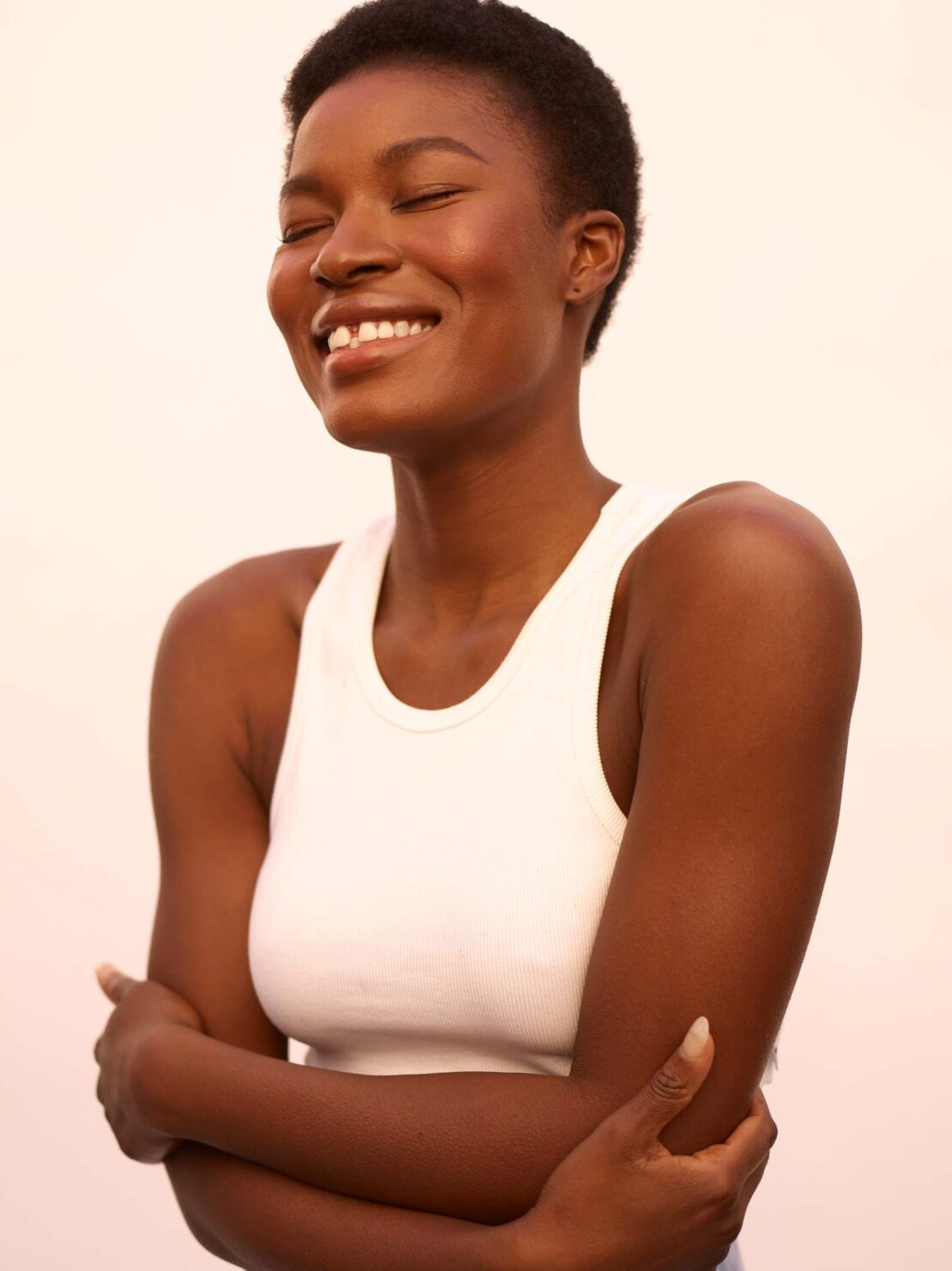 Portrait of smiling Black woman with short hair wearing a white ribbed tank top against a plain light background