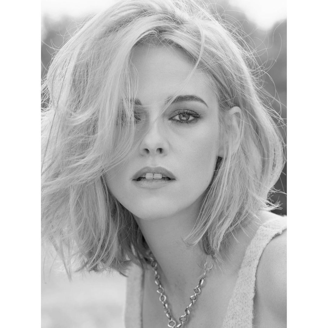 Black and white portrait of a blonde woman with short hair, wearing a necklace and facing the camera with a neutral expression.