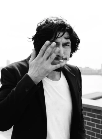 Monochrome portrait of actor Adam Driver smoking a cigarette and raising a hand to his face, photographed by Lauren Dukoff.