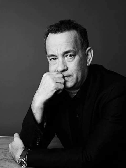 Black and white portrait of adult male in a dark jacket with hand on chin, looking at camera against gray backdrop, wearing wrist watch.